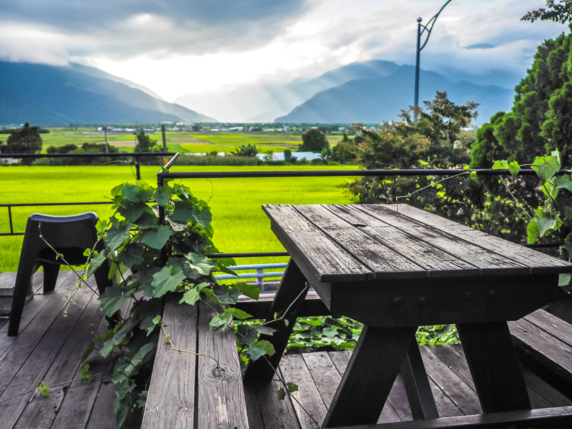 A picnic table on a wooden balcony with a view of bright green rice paddies
