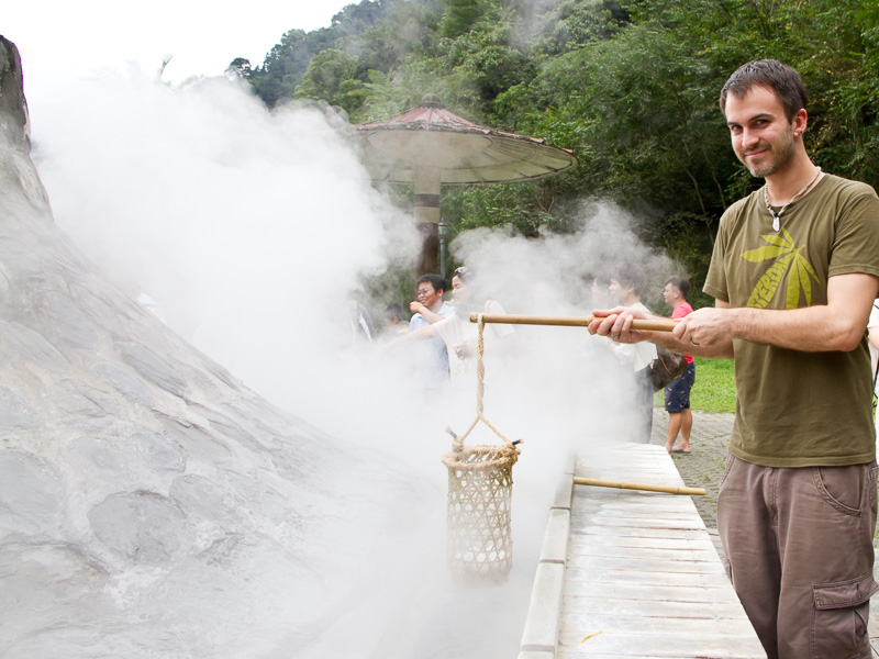 Nick Kembel standing beside a steaming hot spring, holding a basket of eggs on a stick in the hot steam