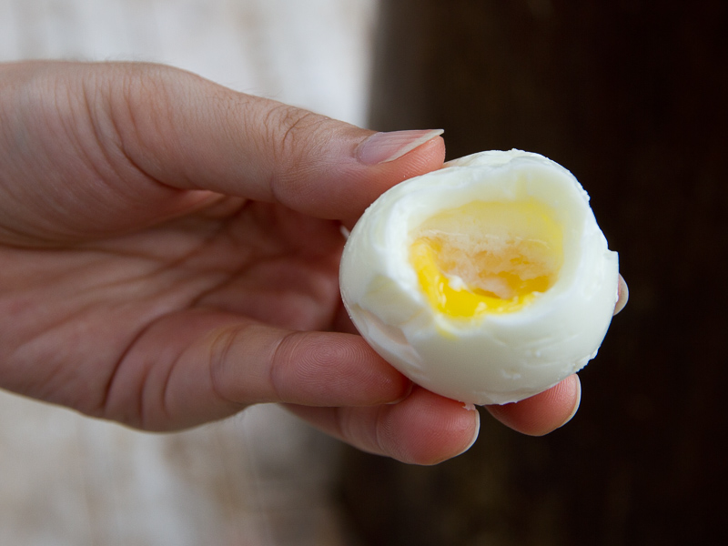 A hand holding up a hot spring egg that is cut in half and has runny yolk inside