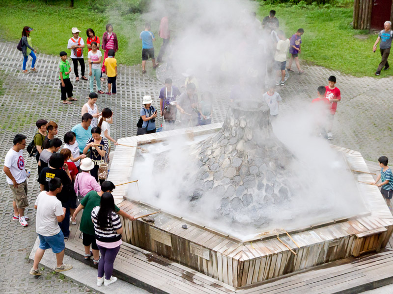 Crowds of visitors standing around a steaming hot spring fountain