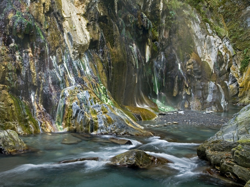 A riverside wild hot spring with colorful cliff walls behind
