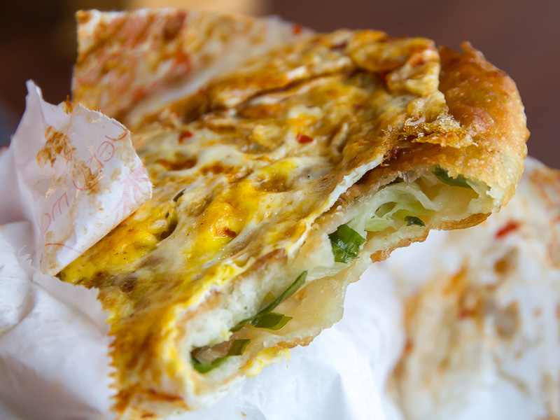 Close up of a green onion cake cooked with egg in a paper bag