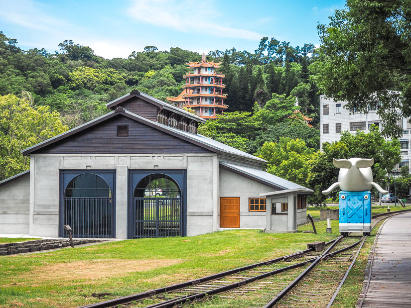 An old train hangar, railway line, whale shaped statue, and shrine on a mountain in the background