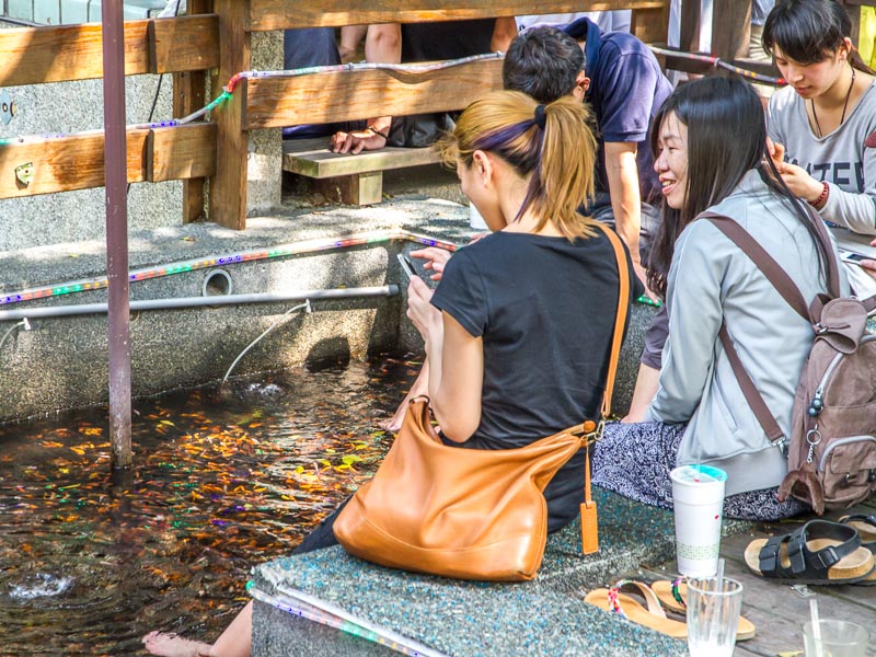 Three Asian travelers sit with their feet in a pond