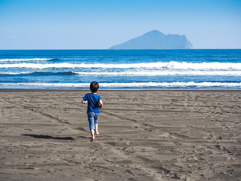 A child running on the beach towards the sea and waves, with a turtle shaped island in off the coast