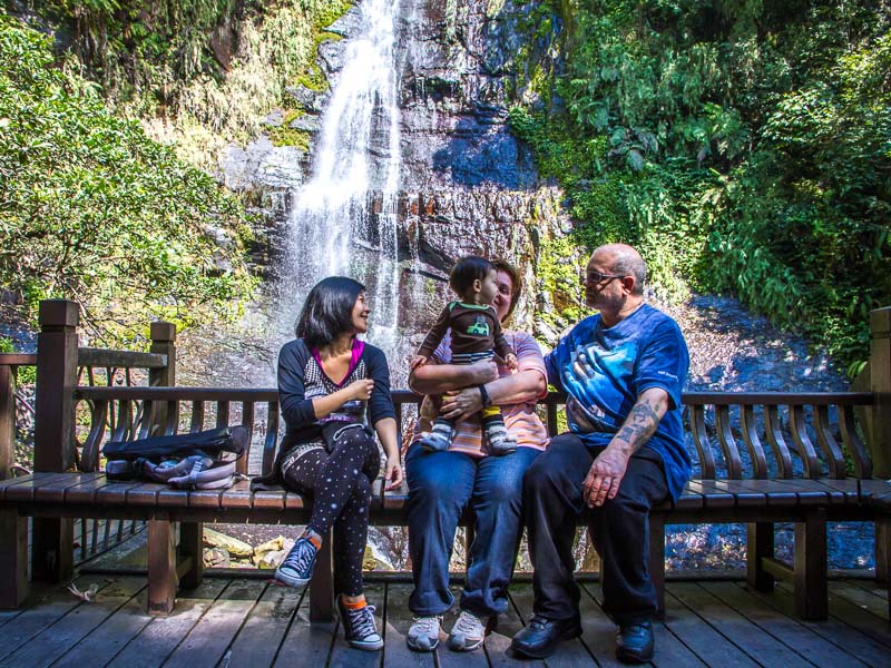 An elderly couple, young Taiwanese women, and her child sitting on a bench with a waterfall behind them