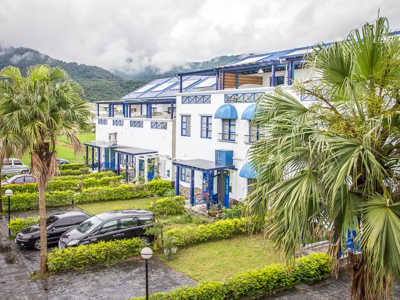 A blue and white hotel building with cars parked in front and trees around it