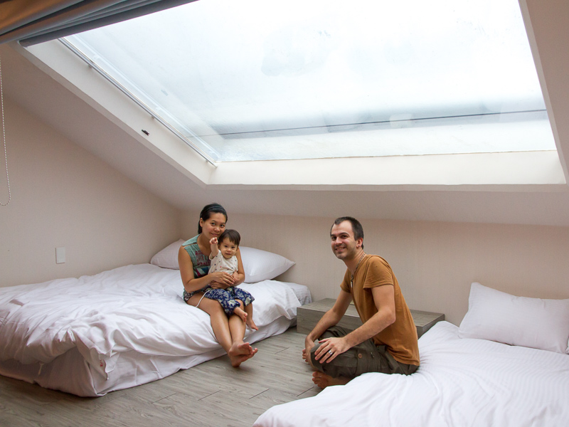 Nick Kembel with his wife and son sitting on the beds inside their guesthouse in Yilan with a slanted roof window above them